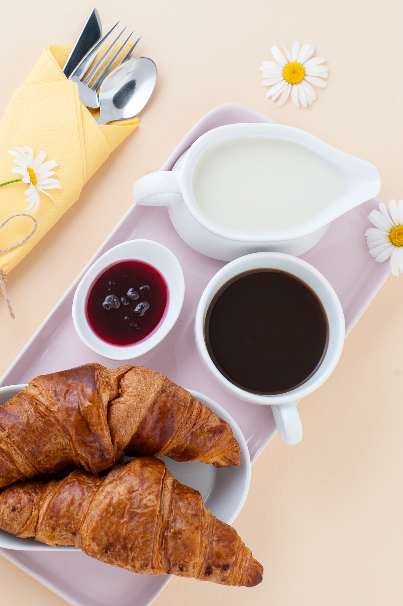 Breakfast consisting of black coffee, milk and a croissant with